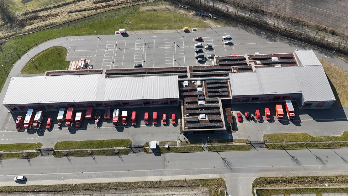 Gebäude von oben, davor stehen Feuerwehrfahrzeuge in rot, dahinter ist ein PKW-Stellplatz